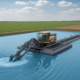 An agricultural lagoon dredge in operation, removing sludge from a large farm wastewater lagoon surrounded by green fields under a clear sky.