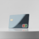 Sleek unbranded metallic credit card with a subtle tricolor accent standing on a minimalist white pedestal against a neutral background, professional commercial photograph