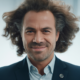 Confident middle-aged man with thick natural hair smiling against white background, representing successful hair transplant result